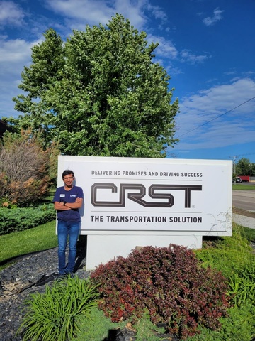Nahar standing next to a sign outside reading "Delivering Promises and Driving Success: CRST - The Transportation Solution"