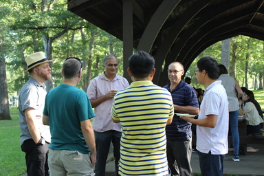 Six faculty chat in a circle next to park shelter