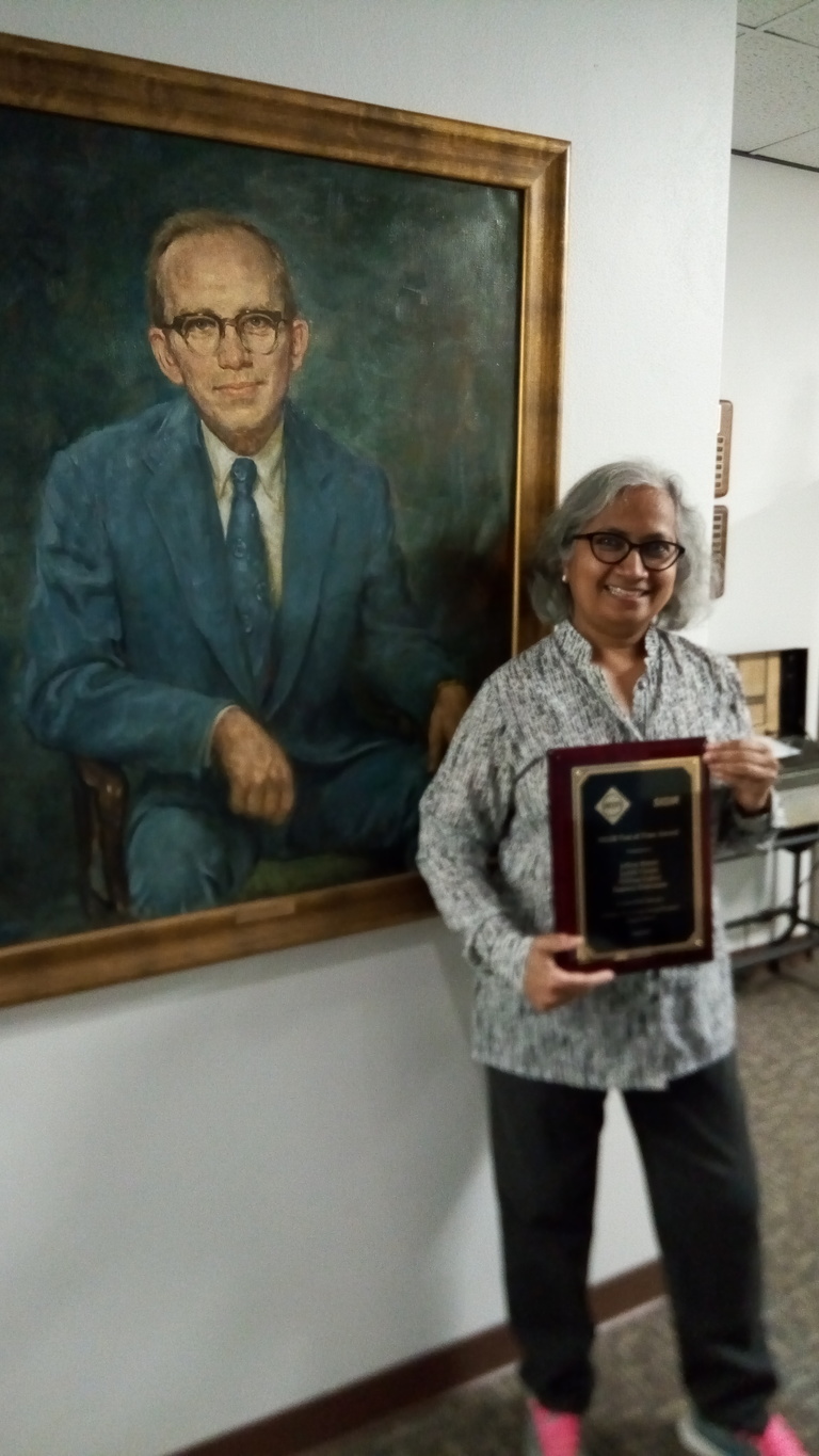 Srinivasan holding congratulatory framed award - standing in front of Gerry Weeg portrait