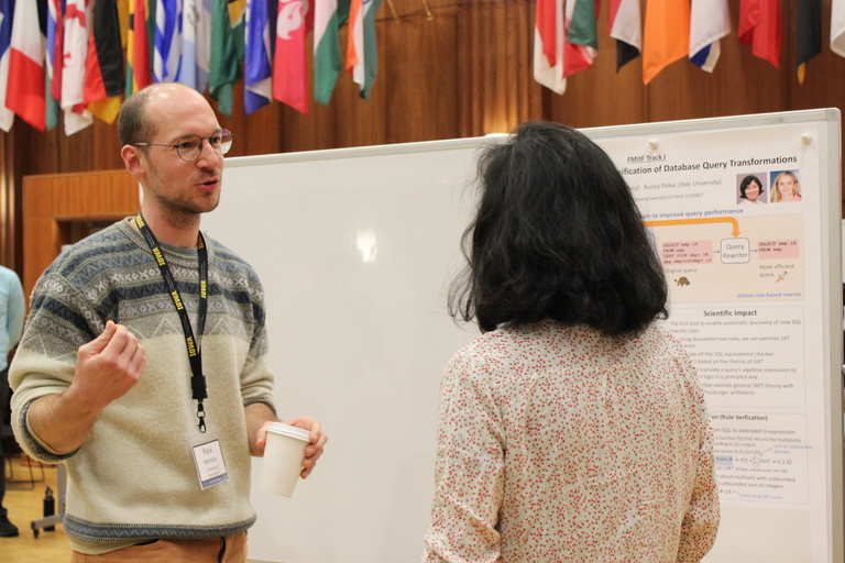 Jinyang Li and Felix Hähnlein talk in front of a poster of Li's research in the IMU's International Ballroom