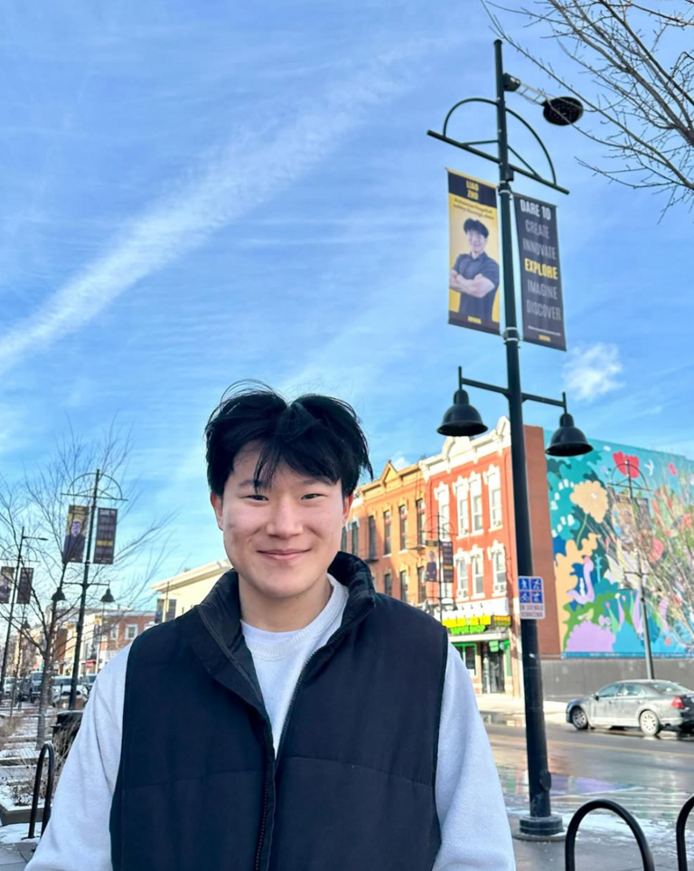 Liao Zhu poses in front of his Dare to Discover banner in downtown Iowa City.