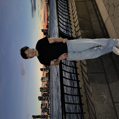 A portrait of Liao Zhu, who is standing in front of a city skyline at sunset.