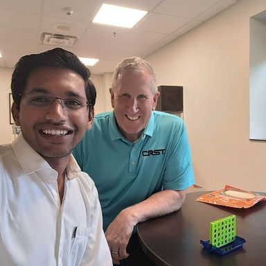Nahar takes a selfie with the new CEO of CRST, Mike Gannon. A mini connect-4 game is on a table in front of the pair.