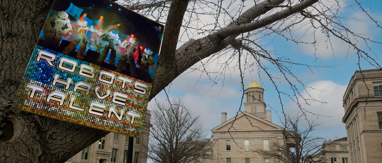 Throwback "Robots have talent" poster perched on UI Pentacrest gingko tree in front of Old Capitol