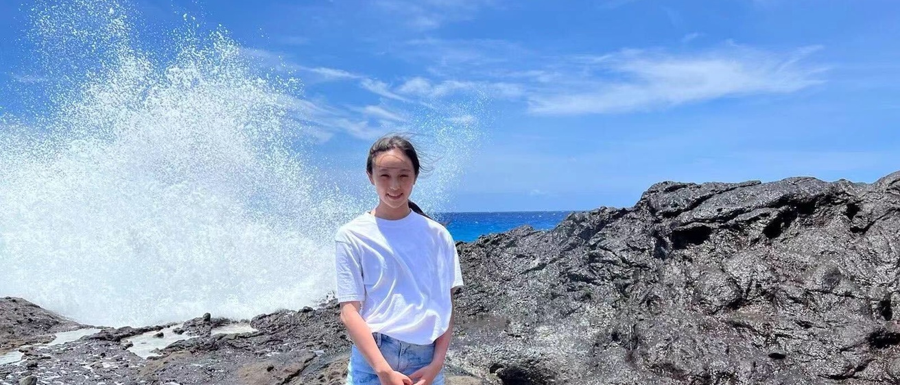 Picture of Rachael Chen on a seaside rocky shore with waves crashing behind her.