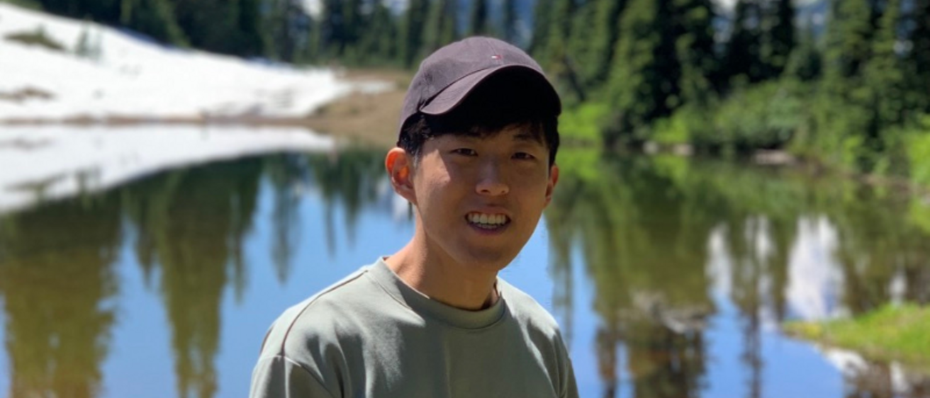 Mingi Lee standing in the outdoors. Above Lee's head is a banner that reads "Congratulations Mingi". The text is surrounded by star icons and a ribbon.
