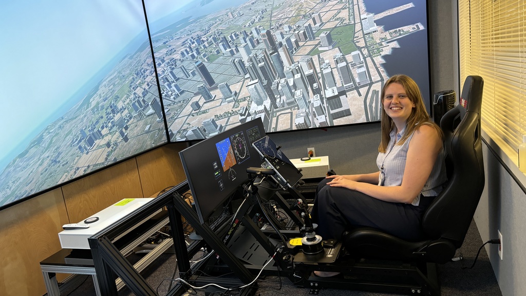 Paulsen sitting in front of two large screens displaying an overhead view of a simulated city and two smaller screens mimicking the dashboard of an aircraft. 