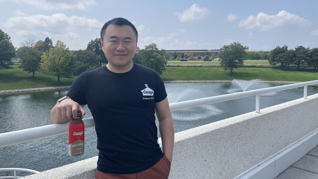 Cai standing on a bridge near Casey's corporate headquarters, wearing a Casey's shirt and holding a Casey's iced coffee
