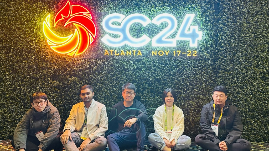 The UIowaCS group for SC'24 poses in front of a neon sign reading "SC'24". From left to right: Yafan Huang, Md Hasanur Rahman, Guanpeng Li, Shihui Song, and Bohan Zhang.